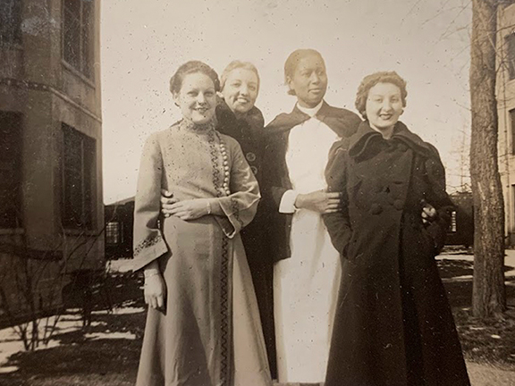 Four nurses standing for a photgraph outside between two buildings